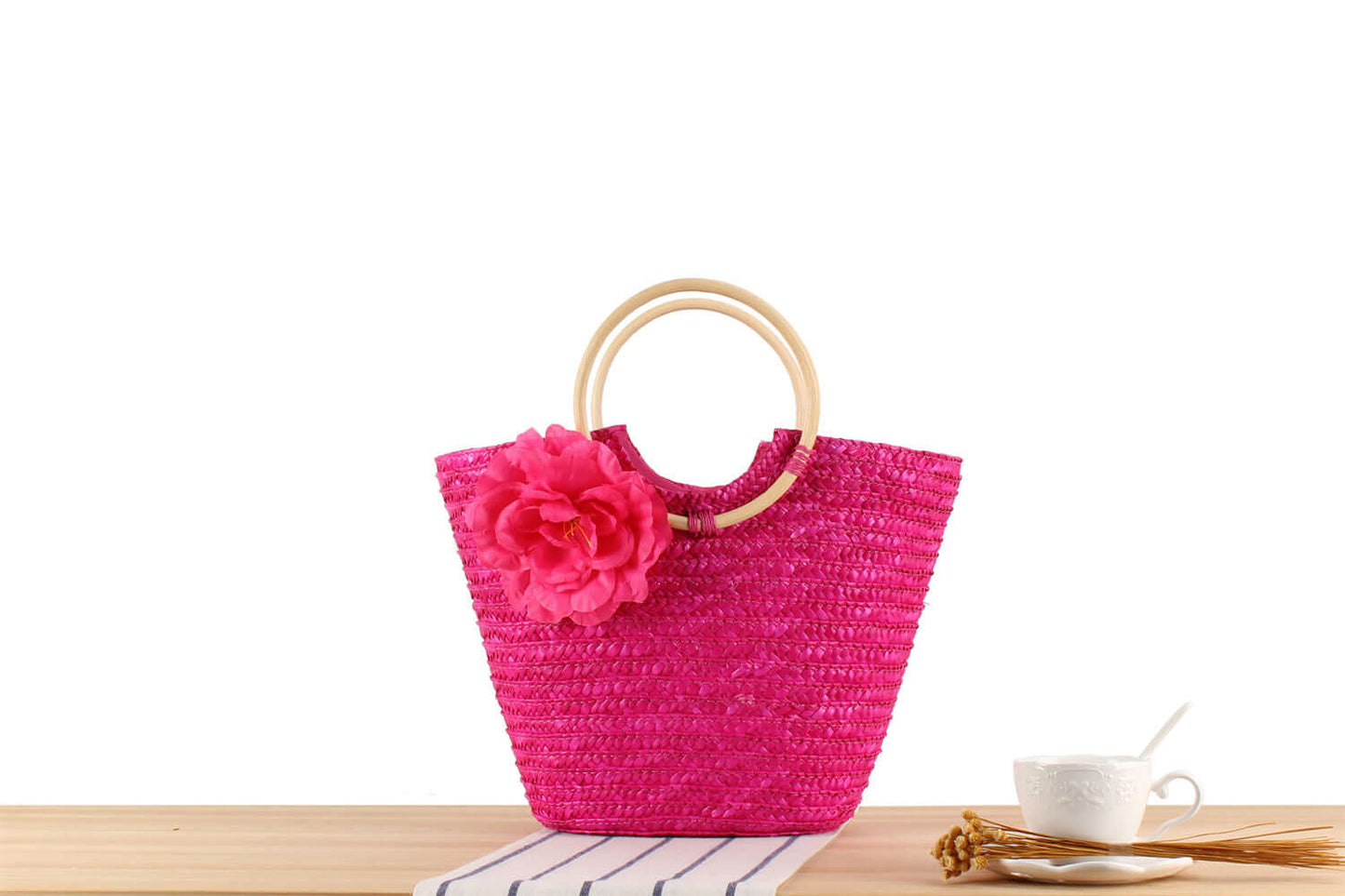 Woven Bag, Straw Bag, Beach Bag in vibrant pink with floral embellishment on a wooden table.