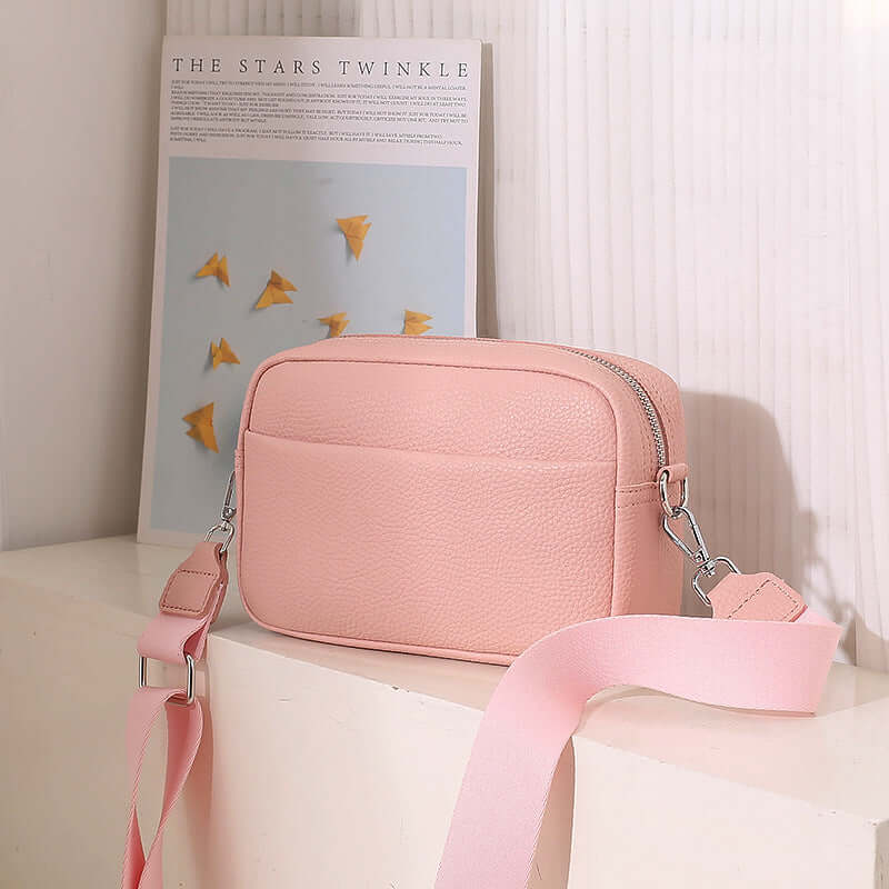 Solid Color Women's Messenger Bag with Wide Strap in pink on a shelf with decorative poster behind it.