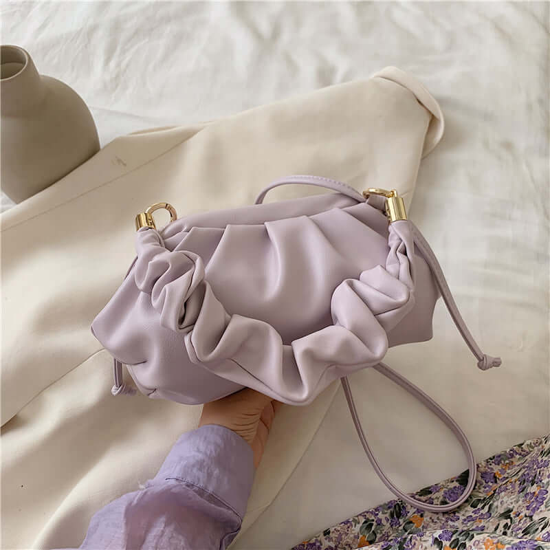 Cloud Bag, Shoulder Bag, Crossbody Bag in lavender with ruffle design and gold accents placed on a soft background.