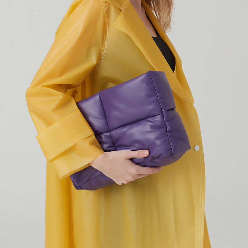 A model holding a purple women's quilted tote bag while wearing a yellow coat.