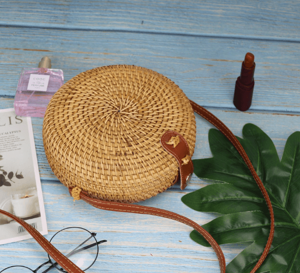 Colorful straw bucket bag on a blue wooden table, surrounded by accessories and greenery, showcasing its round woven design.